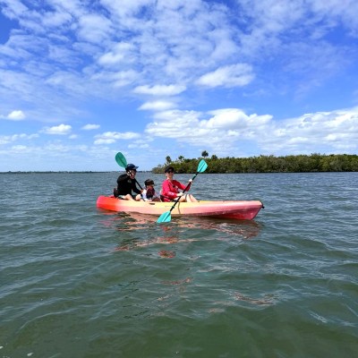 Three people kayaking on a calm lake under a partly cloudy sky.