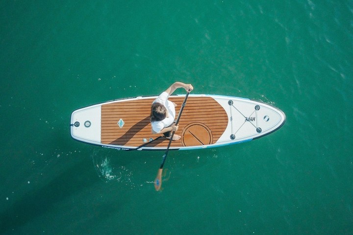 Person paddleboarding on clear blue water from an aerial view.