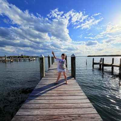 Child posing on a wooden pier under a sunny sky with scattered clouds.