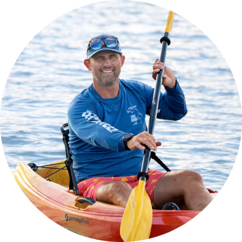 Man kayaking on water, wearing a blue shirt and red shorts.